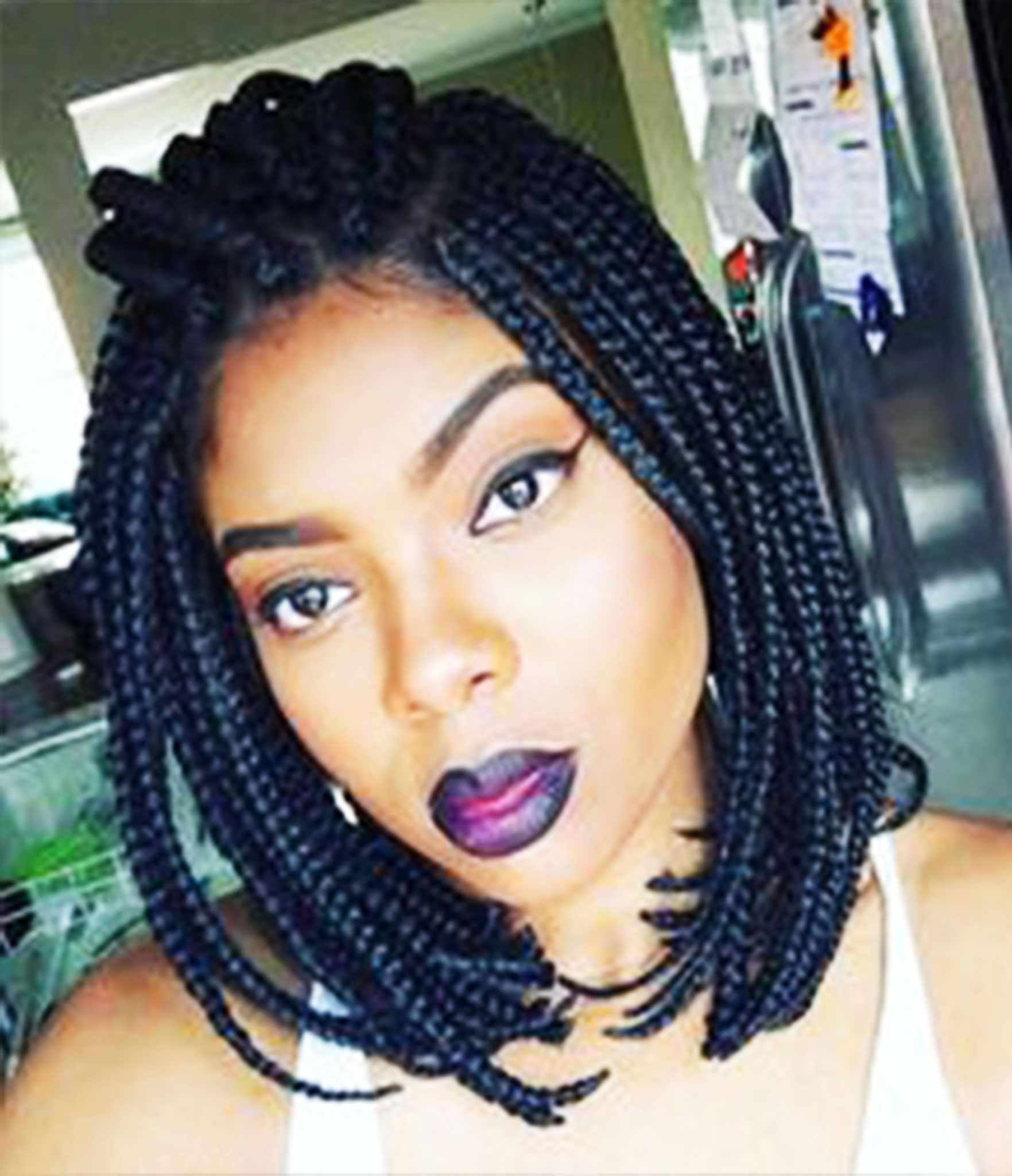 A woman with a dark brown bob with box braids styled into a crown braid and with side-swept bangs